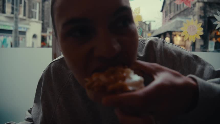 Woman takes a big bite of a snack inside a restaurant decorated with flowers on the windows