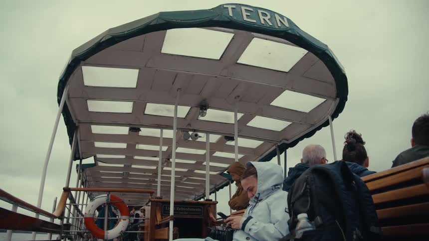 Five person on a boat one is looking at a mobile phone with other people sitting nearby