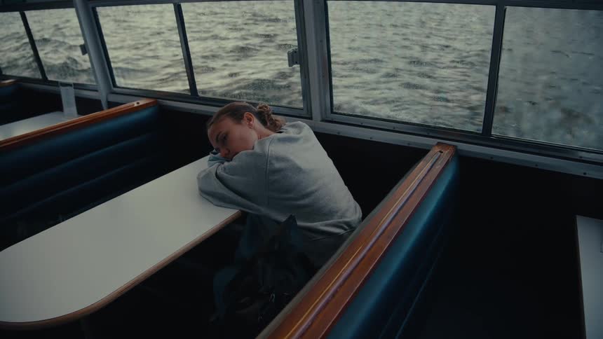 A woman rests her head on a table inside a moving boat