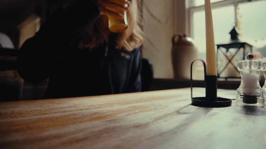 A woman picking up a glass of beer from a table and drinking it then placing a plate with a fork and knife on the table