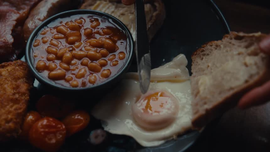 A hand spreads cheese on bread next to a plate of beans and vegetables