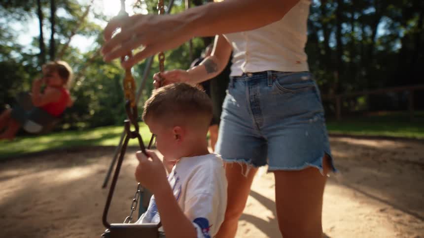 A man and woman push two young boys on a swing set