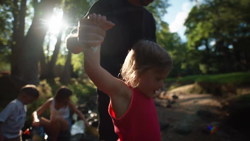 Father holding both hands of his daughter and walking in an outdoor area with trees