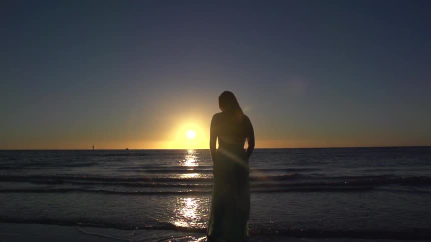 Woman standing by the water at sunset