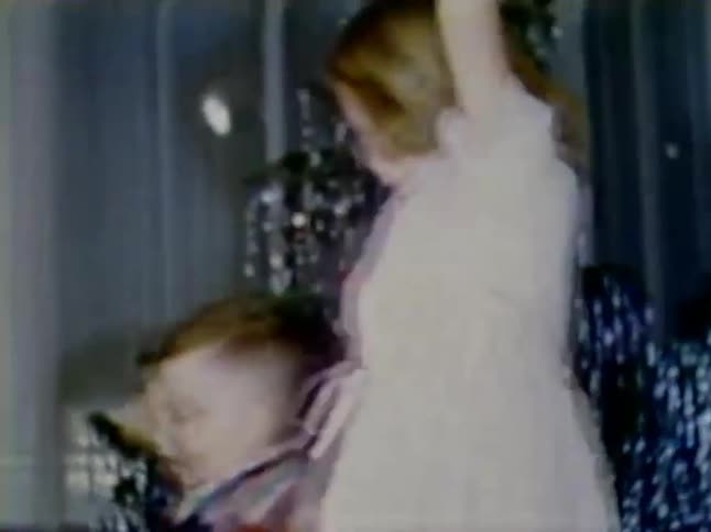 Two children dance in front of a christmas tree