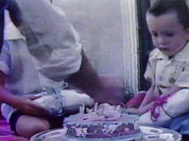 A person lights the candles on a birthday cake as the children watch