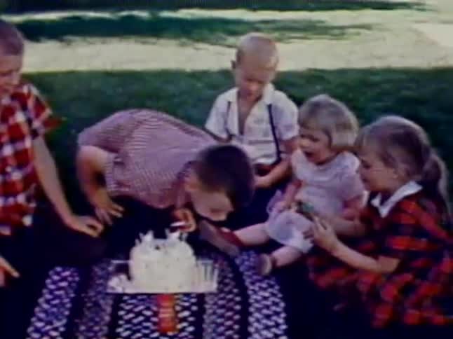 A group of children sit around a birthday cake as the candles are blown out