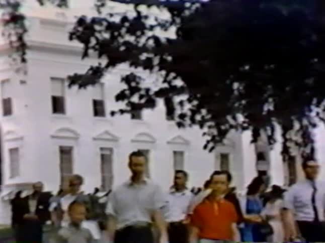 A crowd walks from a large white building