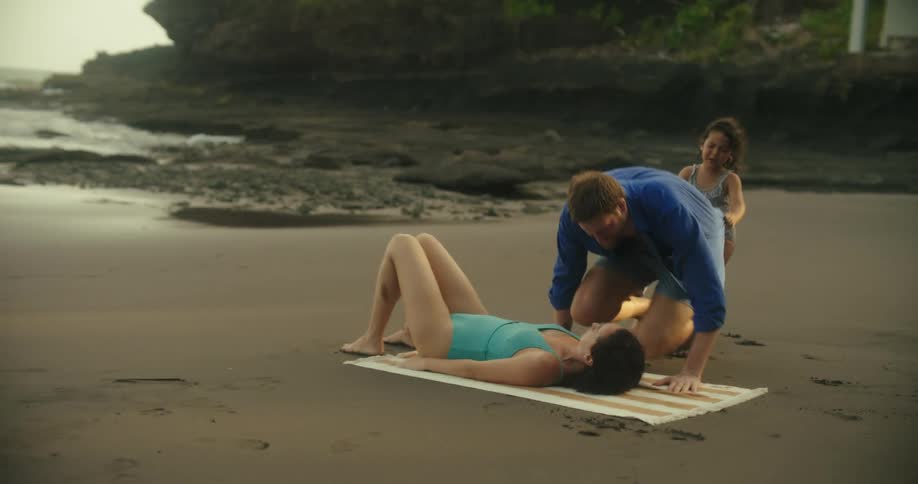 A couple shares a romantic moment on a beach towel by the shore