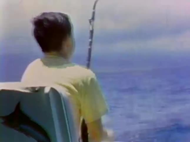 A boy sitting on a boat reels in a fishing line