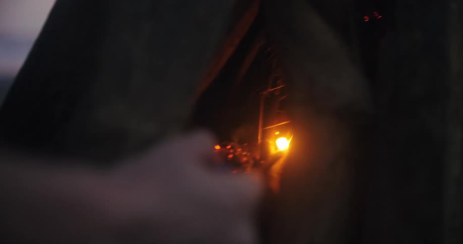 A person uses a lighter to kindle a small fire inside a makeshift fire pit of large logs the flame flickers and grows slowly illuminating the surrounding wood