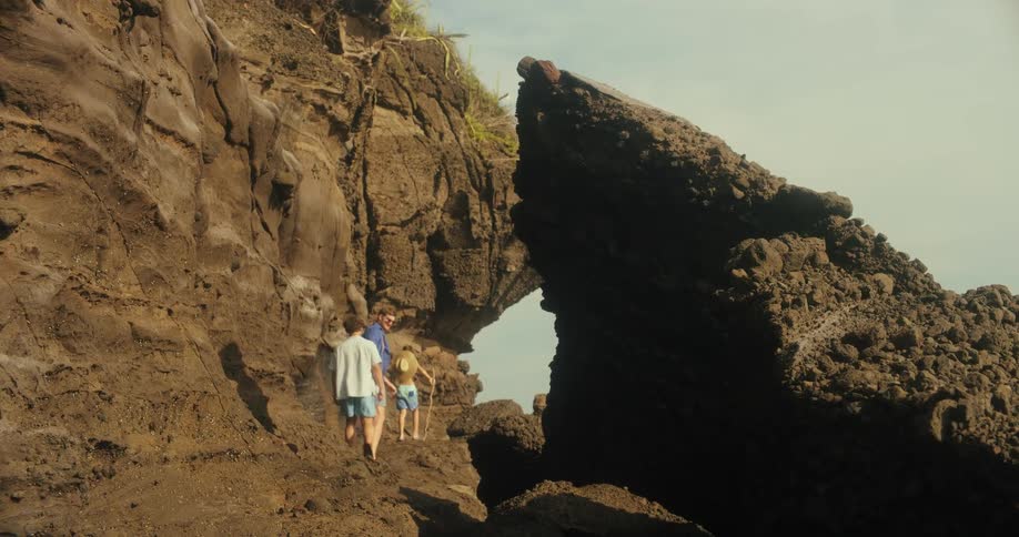 A family explores rocky cliffs by the ocean under a stone arch