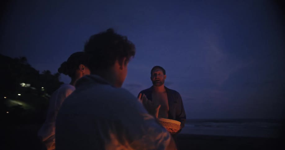 Three people talk while holding marshmallows by a fire at night