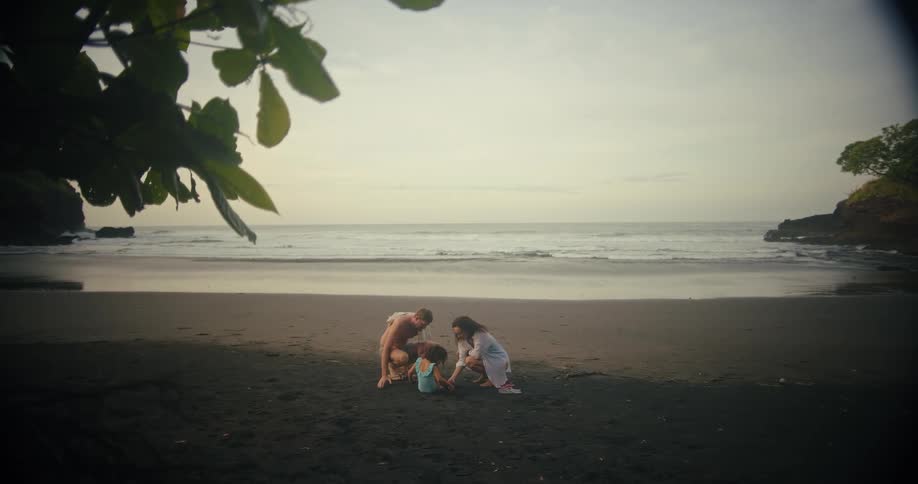 Family consisting of parents andfemale toddler daughter playing with sand at the beach outdoors during dusk or dawn
