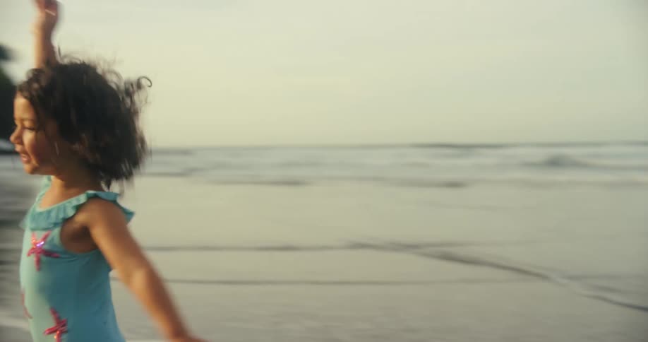 A young girl in a swimsuit runs toward her father on the beach at midday