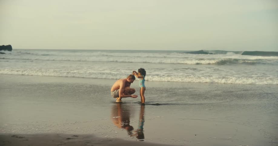 Father and daughter play together on the beach by the shoreline