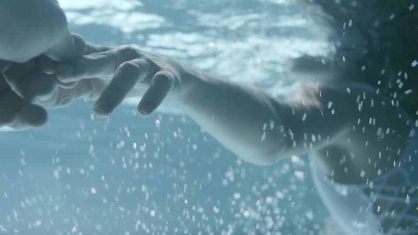 A woman floats on the water holding someone's hand