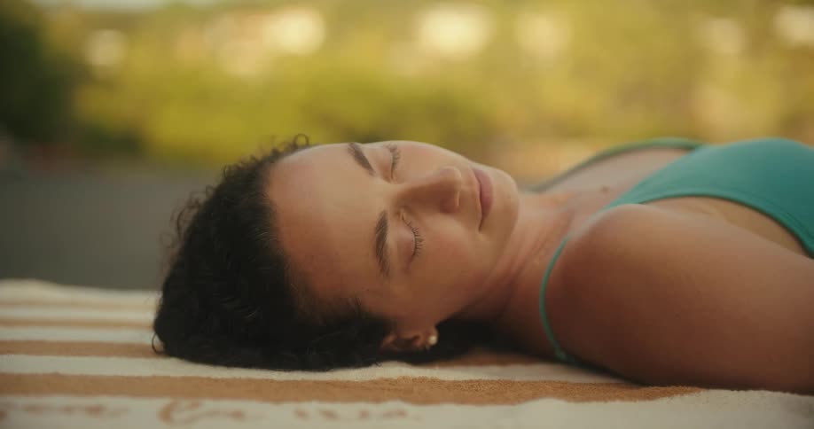 A woman turns her head to one side while resting outdoors with her eyes closed