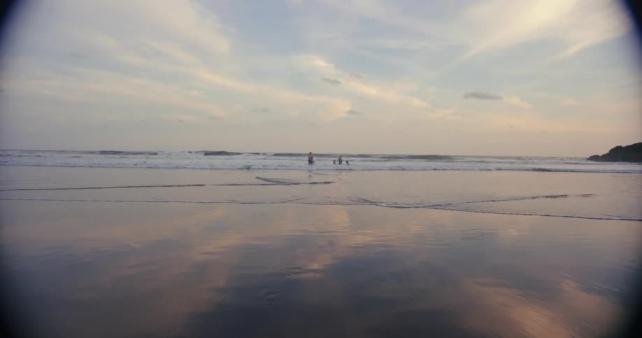 Small group of people at the beach bathing in the sea and playing with the water outdoors during dusk or dawn