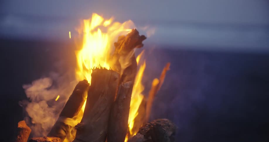 A campfire burns brightly on a beach against the dark night