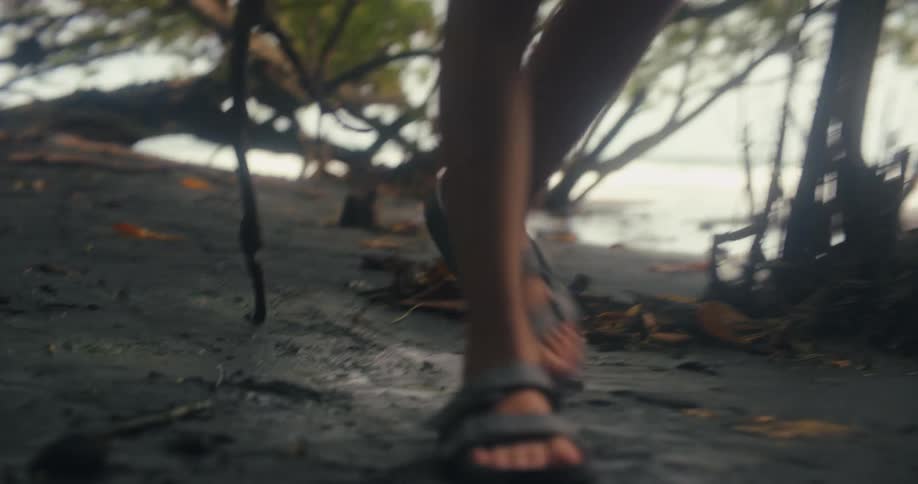 Person walks in sandals on sandy ground with scattered dry branches