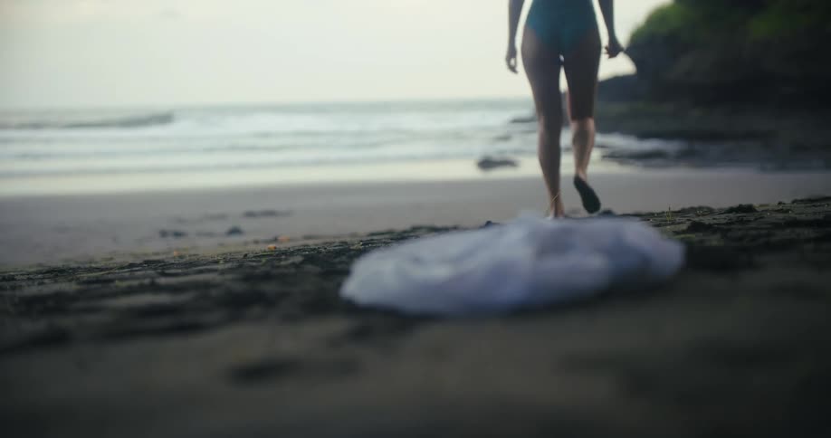 A person whose face is not visible is on a sandy beach they drop a white shirt onto the sand and then walk into the ocean