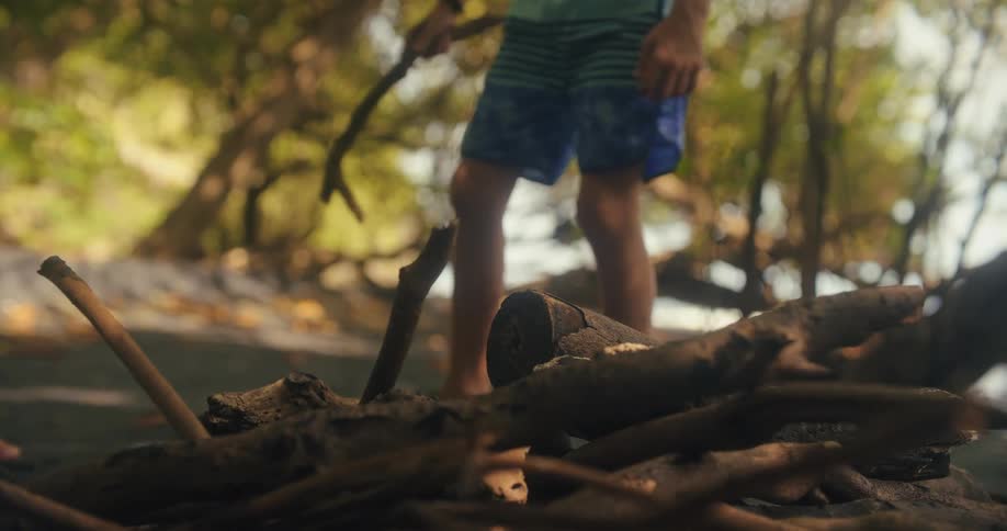 Two young men walk shirtless along a shaded beach path under trees