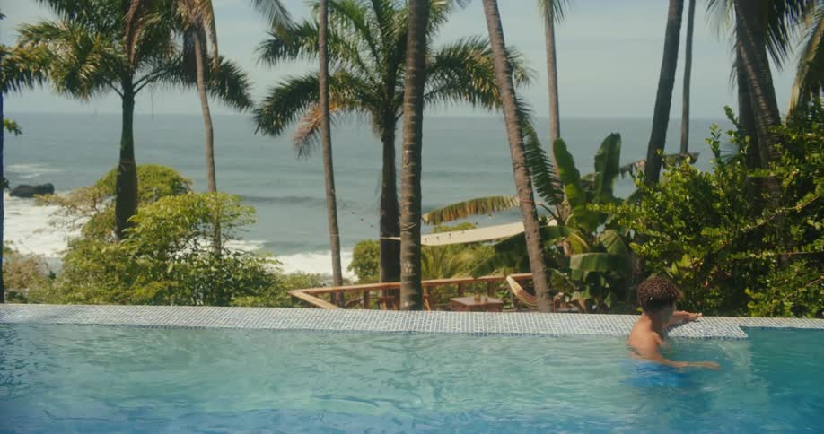 Boy plays at the edge of a pool overlooking the sea and palm trees