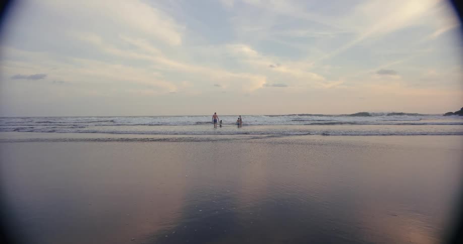 Four people stand together in the shallow waves of the ocean under a pastel sky