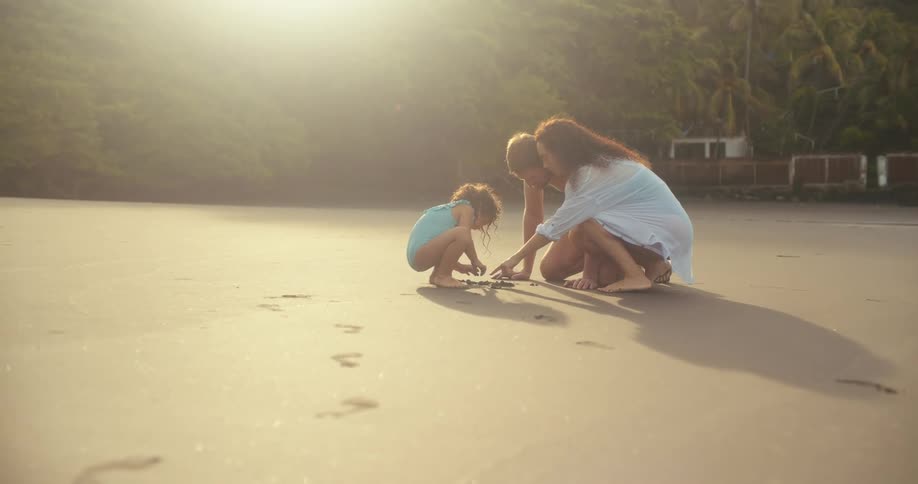 Family with a child kneeling on beach drawing on the sand