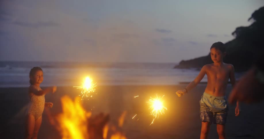 Family plays with sparklers while standing around a fire on the beach in the evening