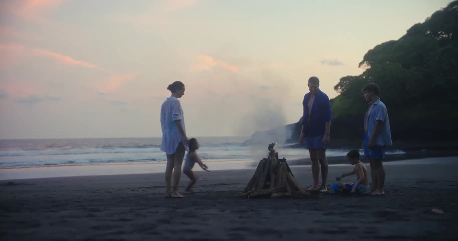Family gathered around a bonfire on the beach at sunset