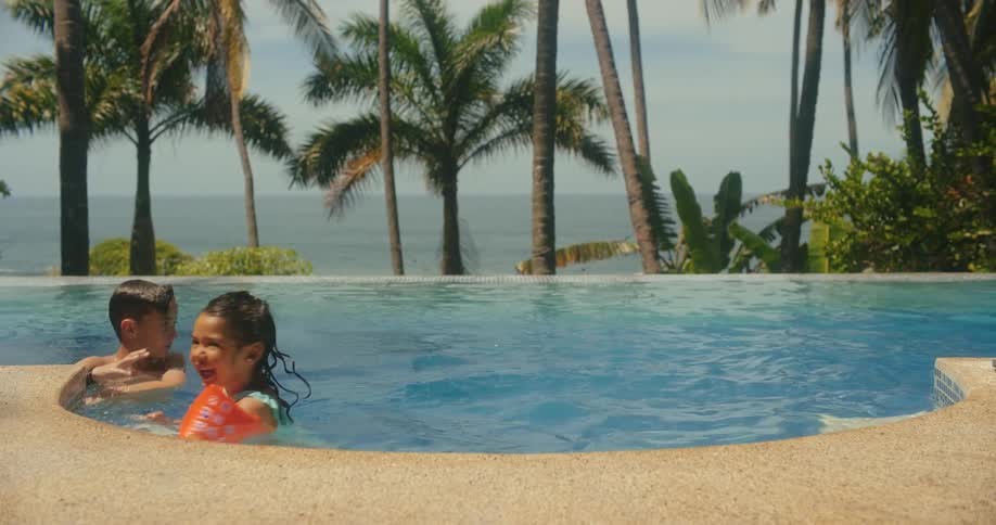 A girl with floaties stands in a pool with a boy then the girl leaves the pool