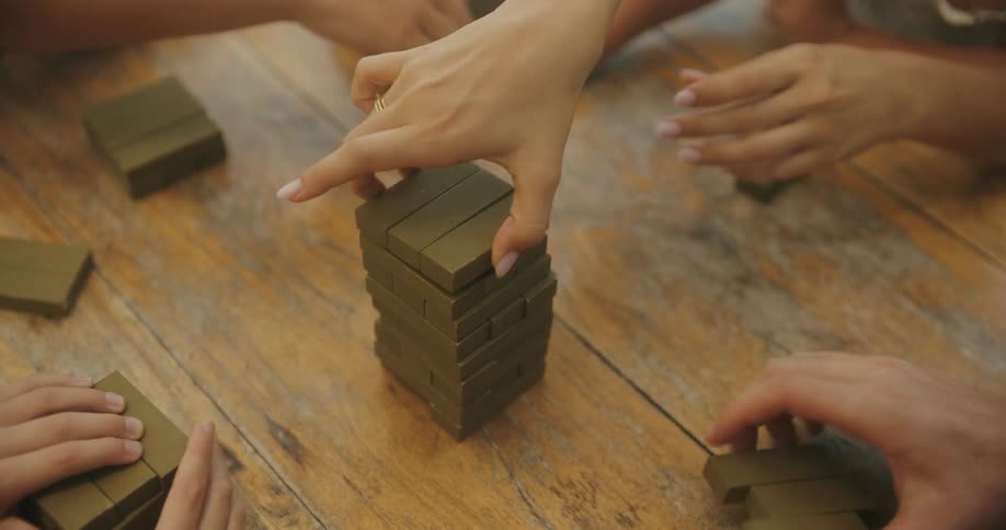 Several hands are engaged in a blockstacking game on a wooden table