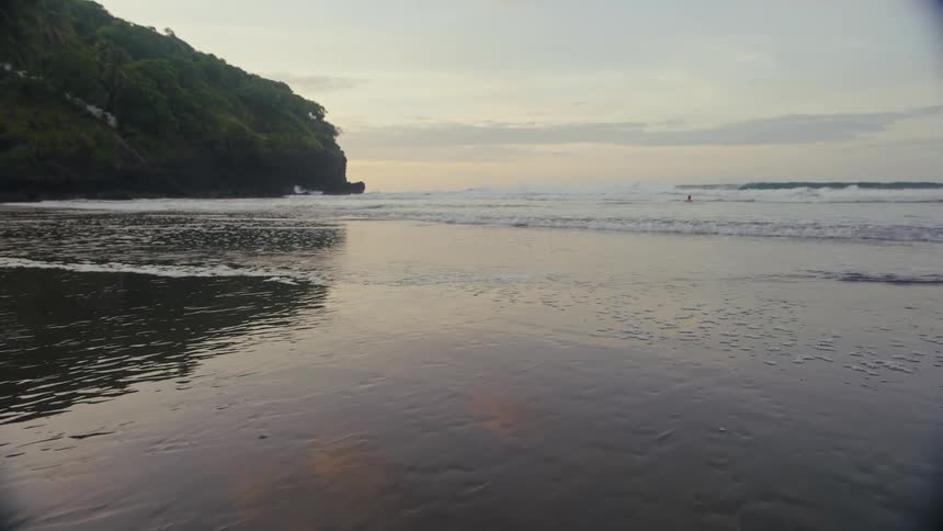 Ocean waves wash upon a sandy beach under a dimly lit sky
