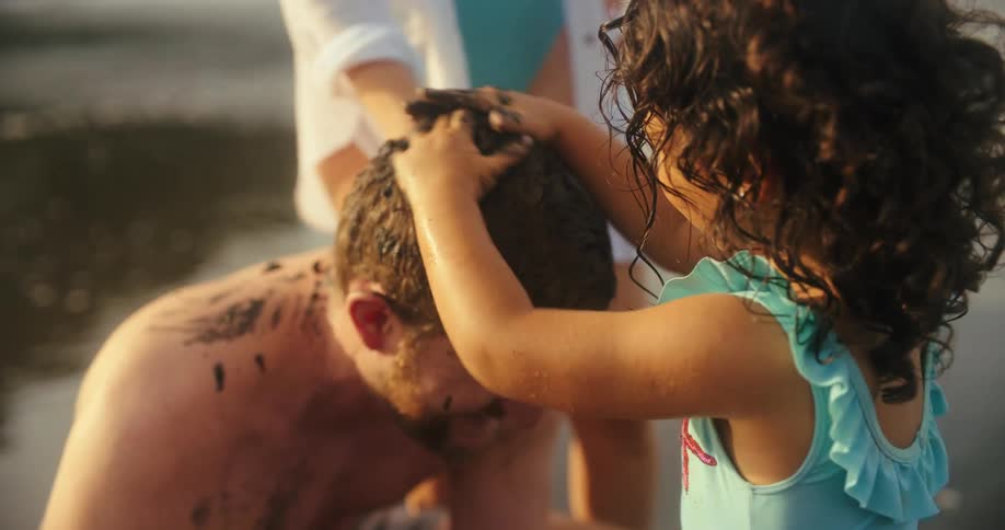 A little girl playfully puts mud on her fathers head at the beach