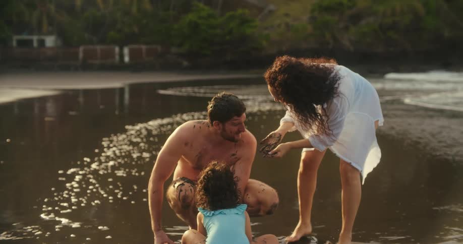 A family plays as a child covers an adult with sand on the beach