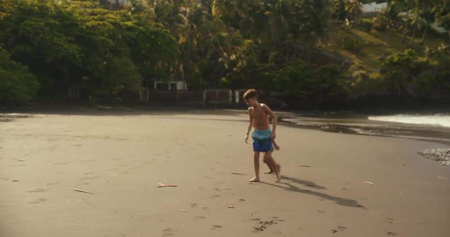 Two children run across the sandy beach towards the sea