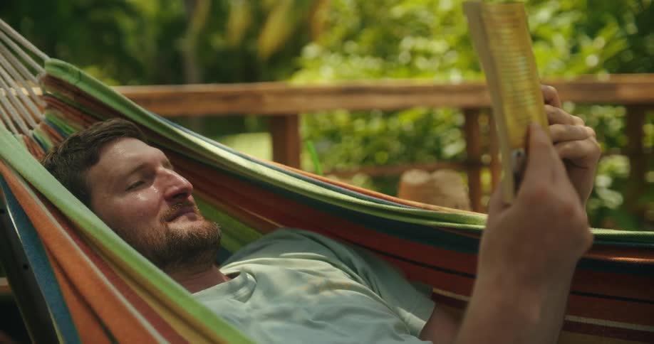 Man relaxing in a hammock in the backyard reading a book
