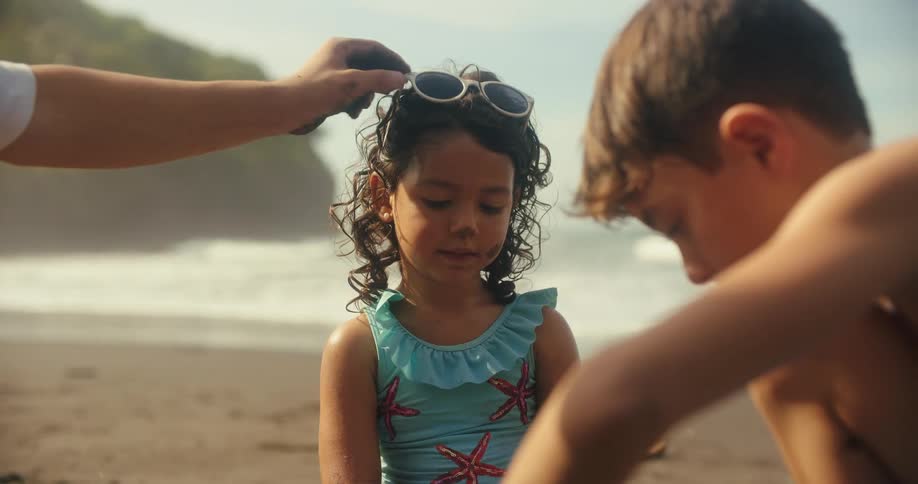 Female toddler playing with a male child and a male teenager at the beach by building a sandle castle in the sand then tearing it down outdoors during day time