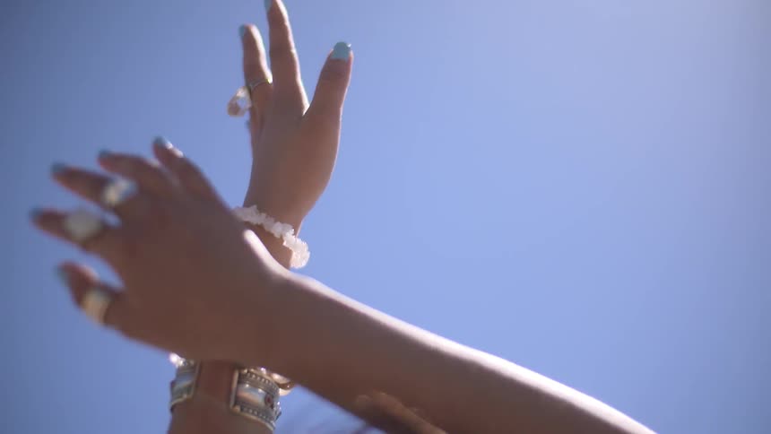 A woman with numerous rings on her fingers, and bracelets on her wrists, raising her arms towards the sky and moving them as if she is dancing