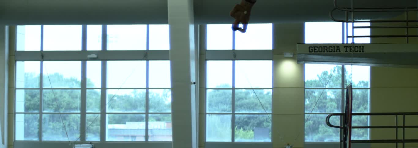 Competive diver diving off high dive indoors and spinning in mid air in slow motion