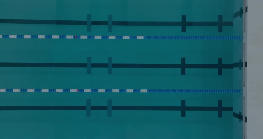 From a high angle the video shows the clear blue water of a swimming pool the pool is divided into lanes by floating lane lines which are white and blue