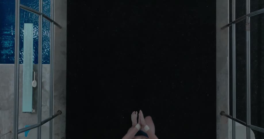 Overhead of a swimmer on a dark platform beside the pool caught midstride