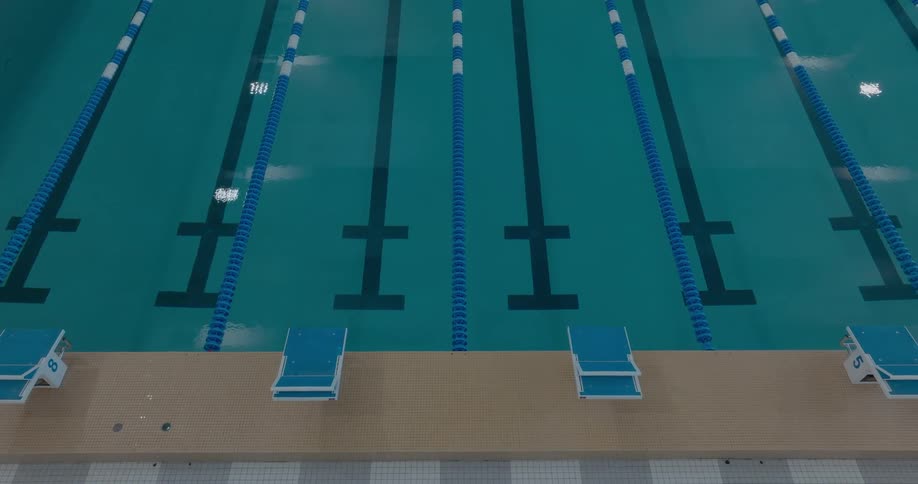 The camera looks down on a swimming pool showing the starting blocks and the lines in the lanes