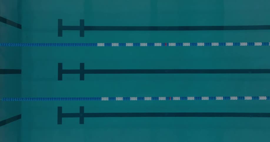 An elevated view shows a competition swimming pool with four dark lanes separated by blue and white lane dividers with several starting blocks visible along the left side