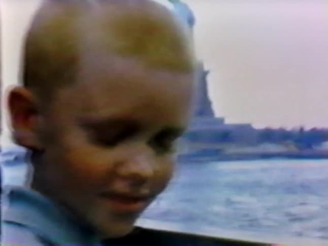 A boy turns around in front of the statue of liberty