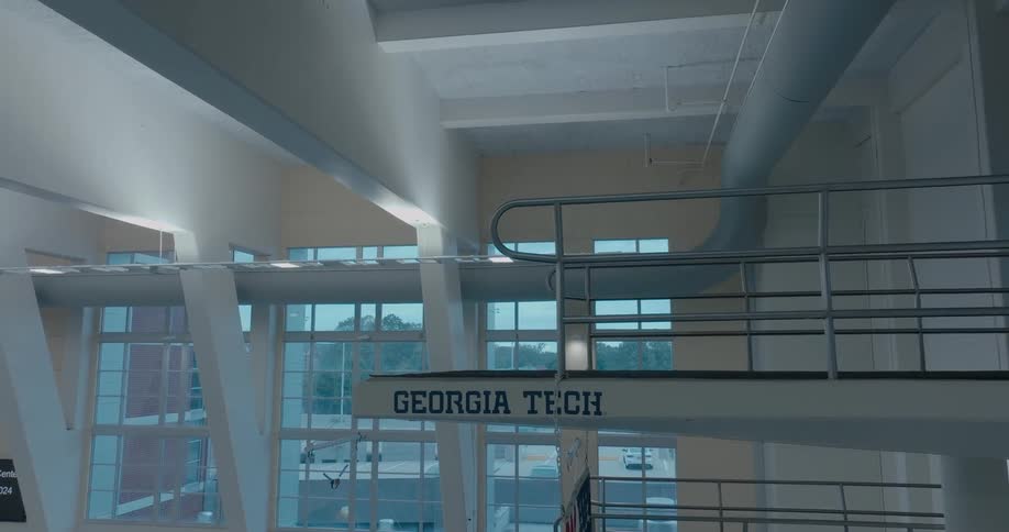 A close view shows a diving board with the words georgia tech on its side as the camera slowly pans across the interior of a large high ceiling aquatic center with long windows