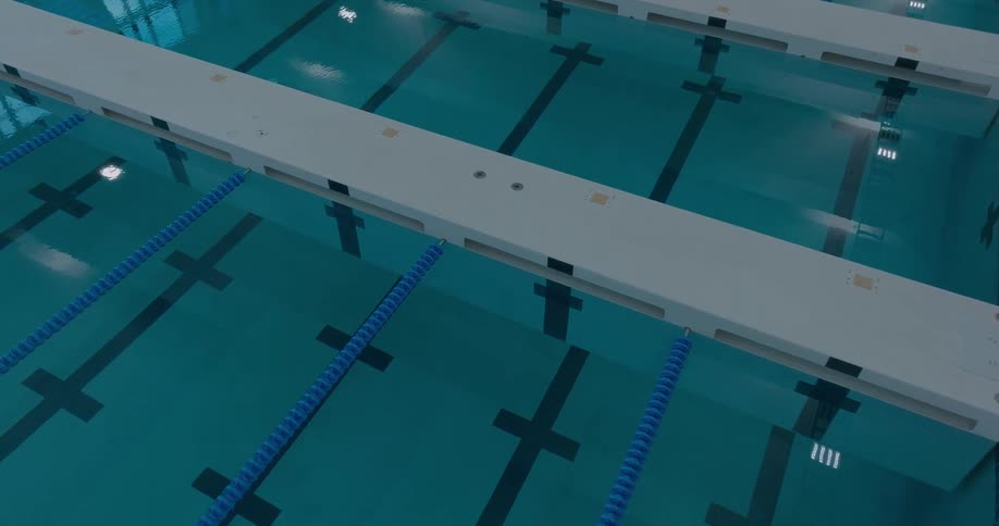 A lowangle shot captures the still serene surface of an olympicsize swimming pool the camera pans slowly from the diving board area across the calm water with the sun reflecting off the surface