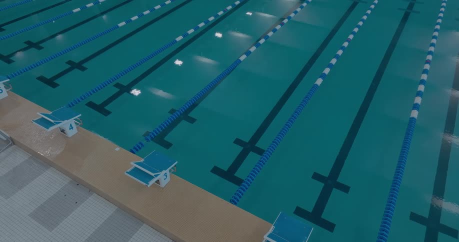 Empty competition pool with numbered starting blocks overlooks crisp blue lanes and calm reflective water
